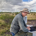 Researcher in field working on laptop