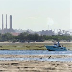 Fishers next to seagrass with industrial facility in the background