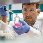 Scientist pipetting into a glass bottle wearing protective gloves and glasses.