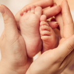 Hands of a midwife holding the feet of a newborn baby